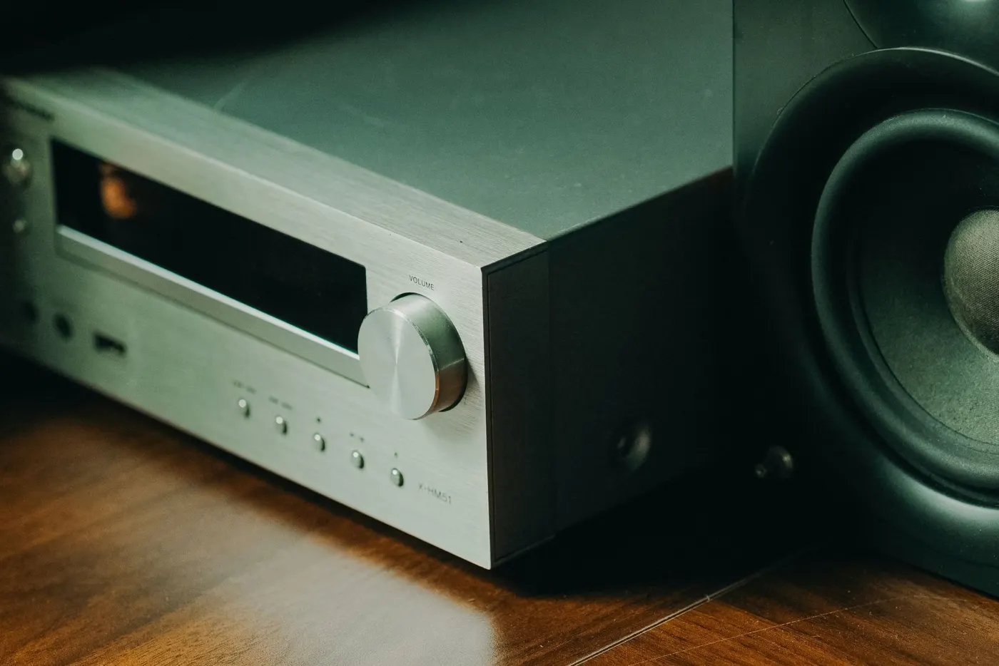 An AV receiver beside a speaker on a wooden shelf.