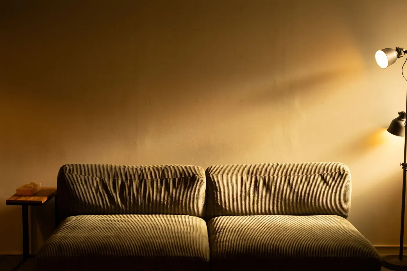 A corduroy sofa beside a glowing floor lamp in a warm living room.