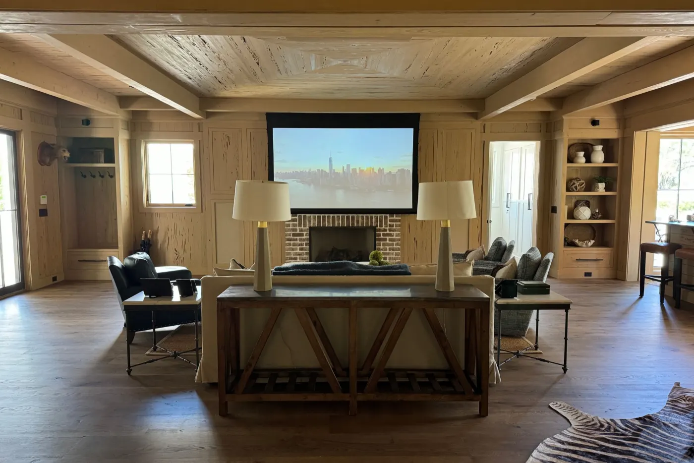A wood-panelled living room with a projection screen above the fireplace and a sofa and armchairs facing it.