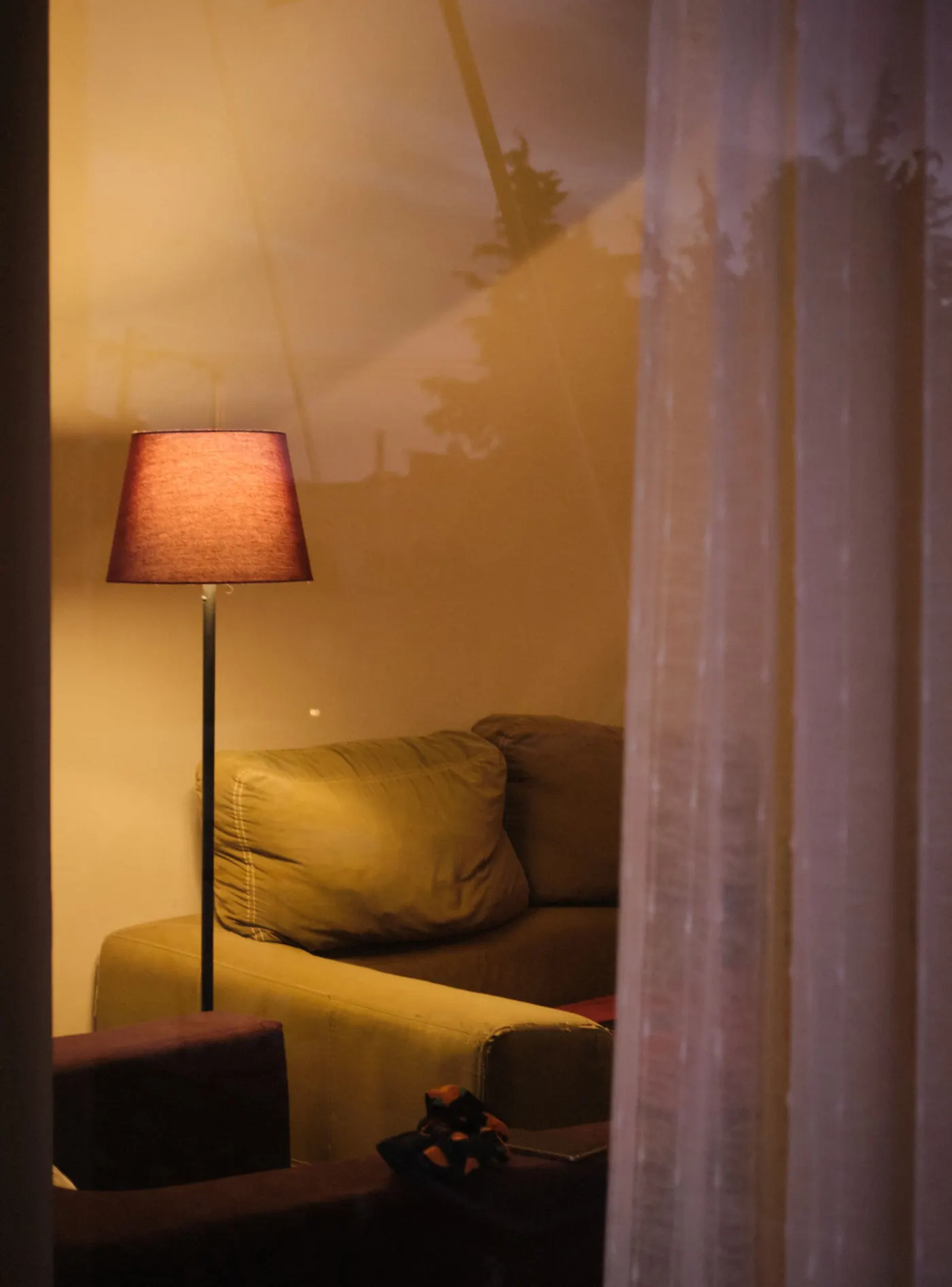 An intimate living room with a warm lamp, sofa and sheer curtains.