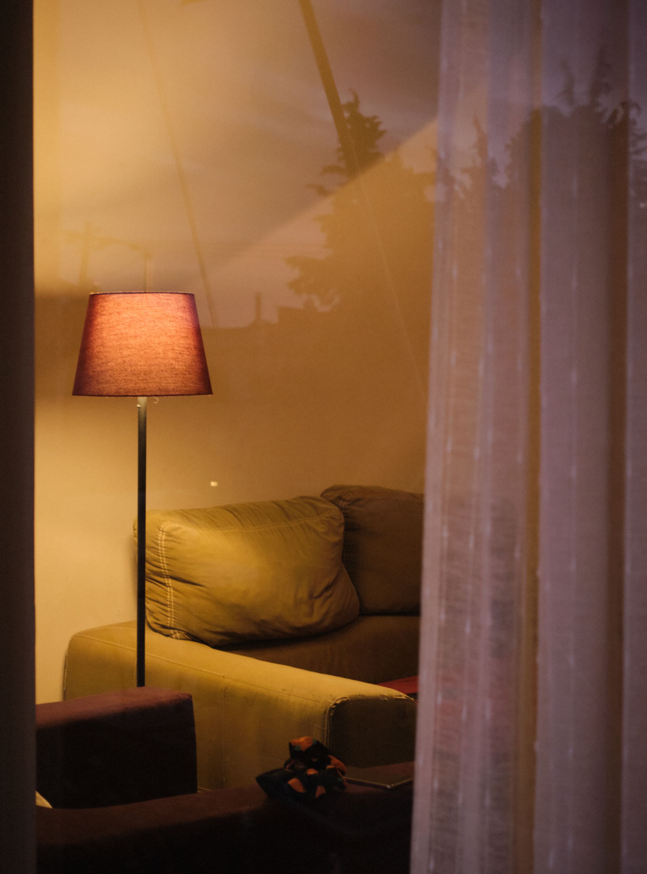 An intimate living room with a warm lamp, sofa and sheer curtains.
