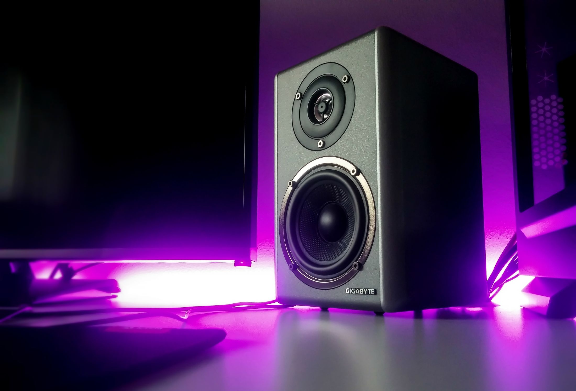 A black loudspeaker illuminated by soft violet light.