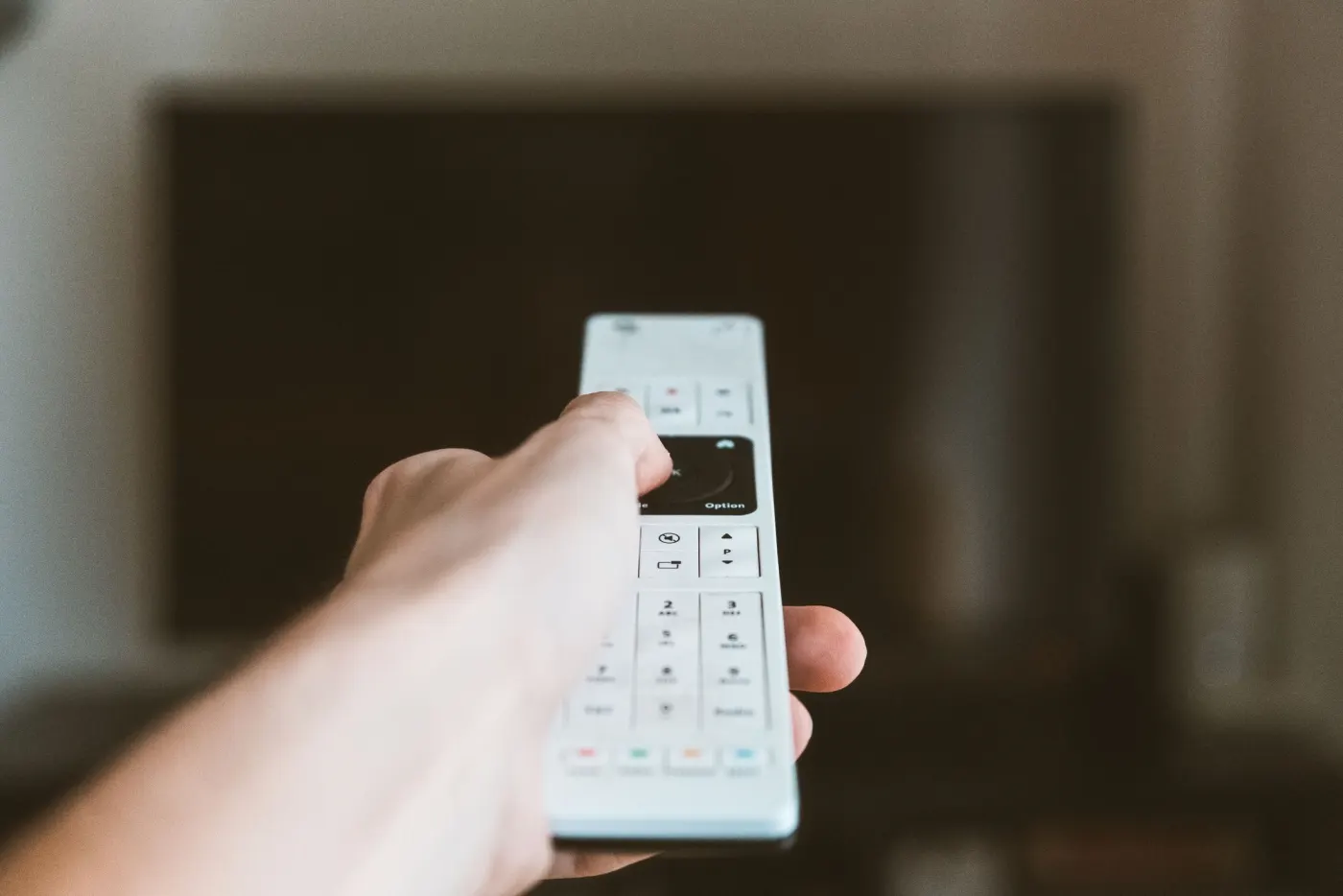 A hand pointing a remote control at a television.